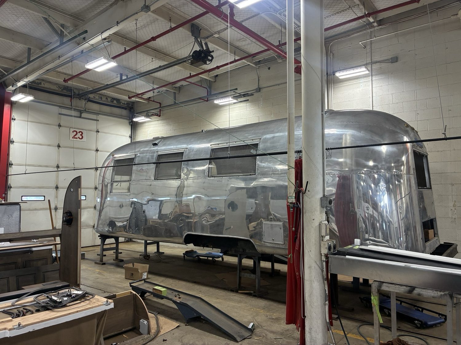 The Silver Bullet Airstream sitting on steel stands inside the Airstream service center in Jackson Center, Ohio, its polished shell lifted clear of the floor with the frame work underneath complete.