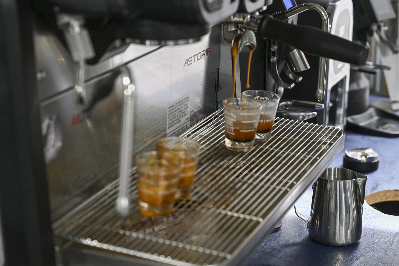 The espresso bar mid-service, with pulled shots on the drip tray, a steaming pitcher, and a tamper on the counter.