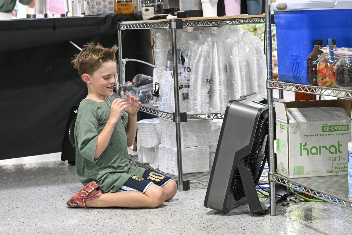 A young member of the crew sitting on the floor behind the service area with a drink, cooling off in front of a fan.