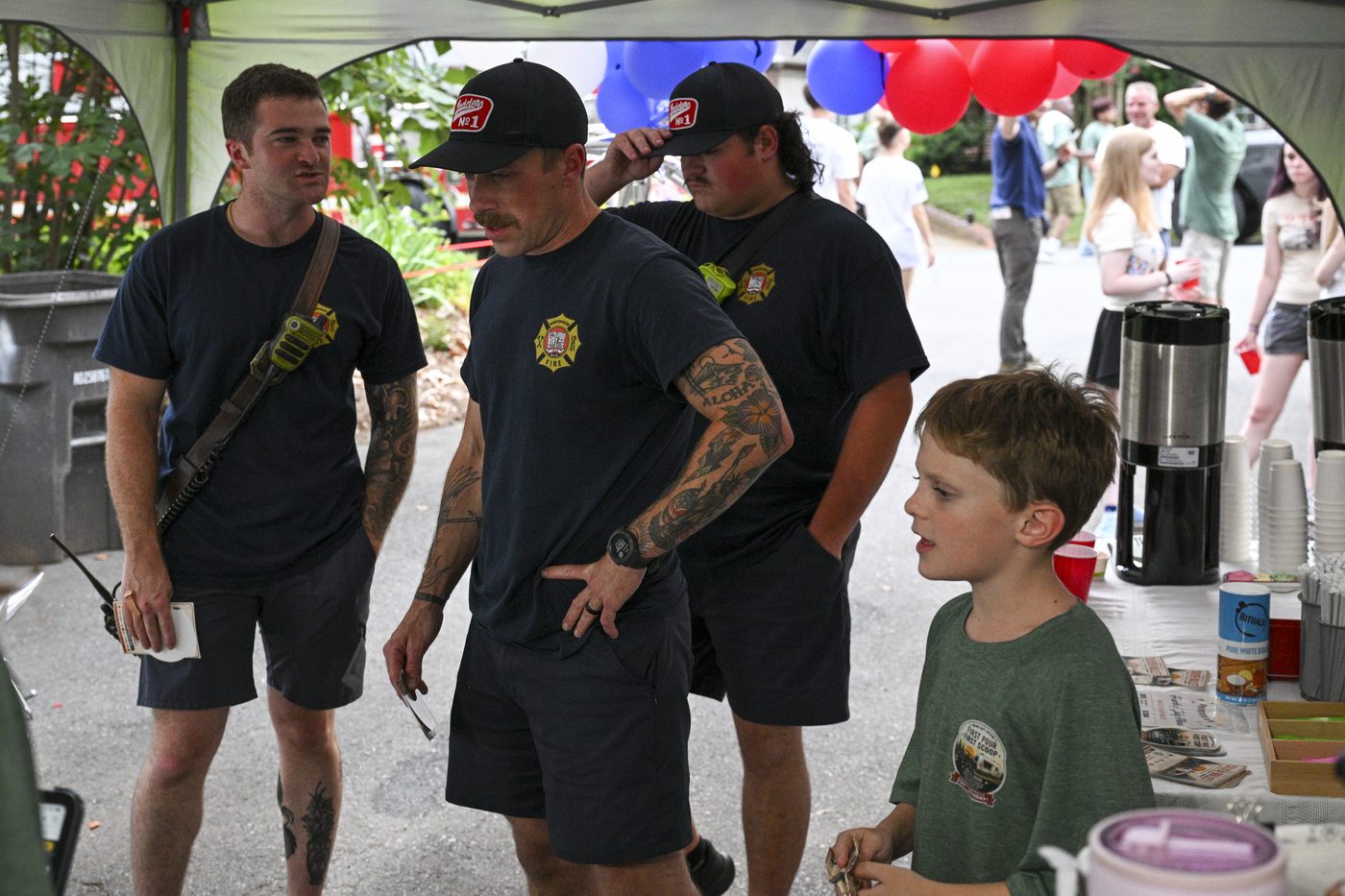 Winston-Salem Fire Department firefighters standing under the tent at the soft opening, talking with a young member of the crew.