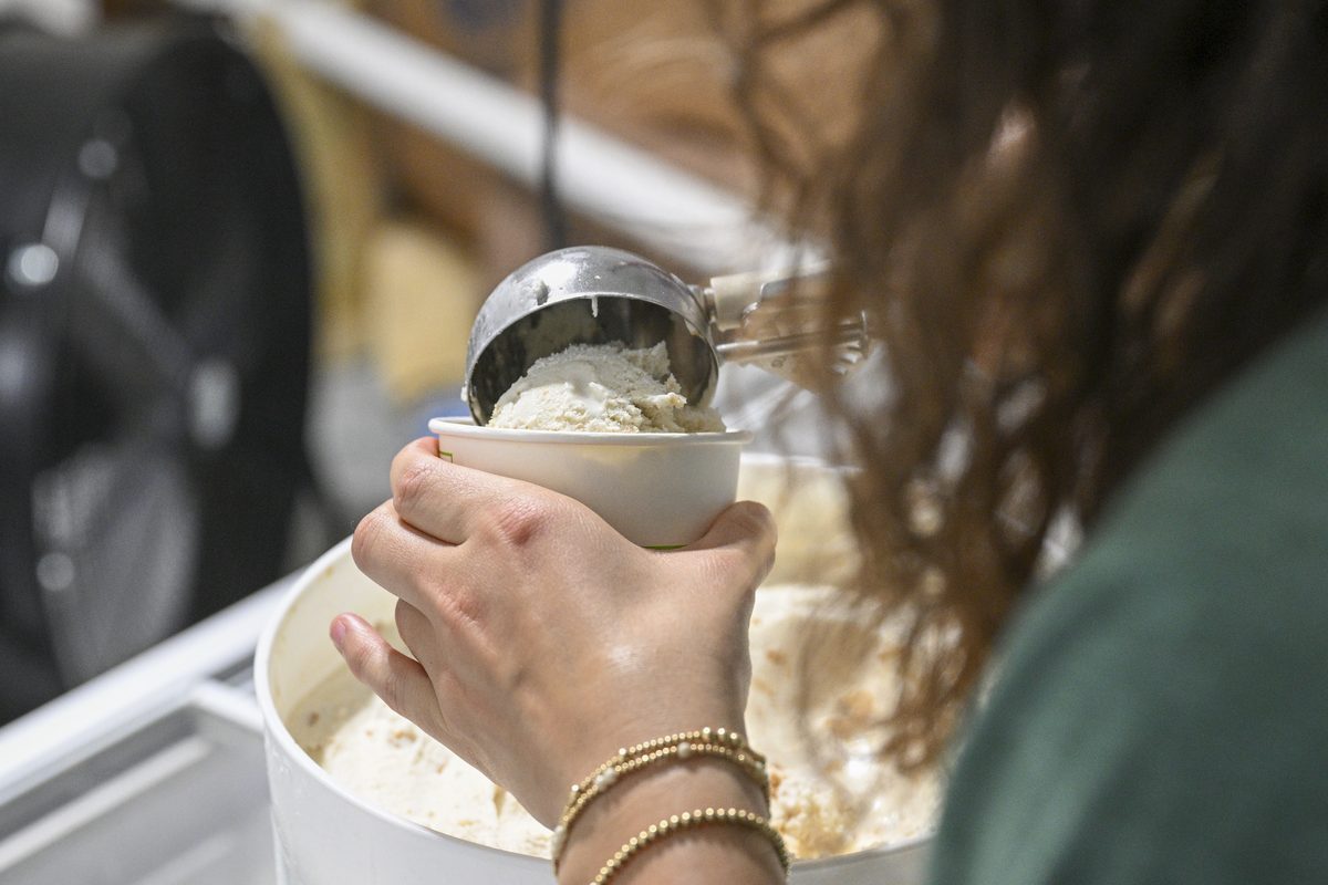 A hand scooping ice cream into a paper cup from an open tub.