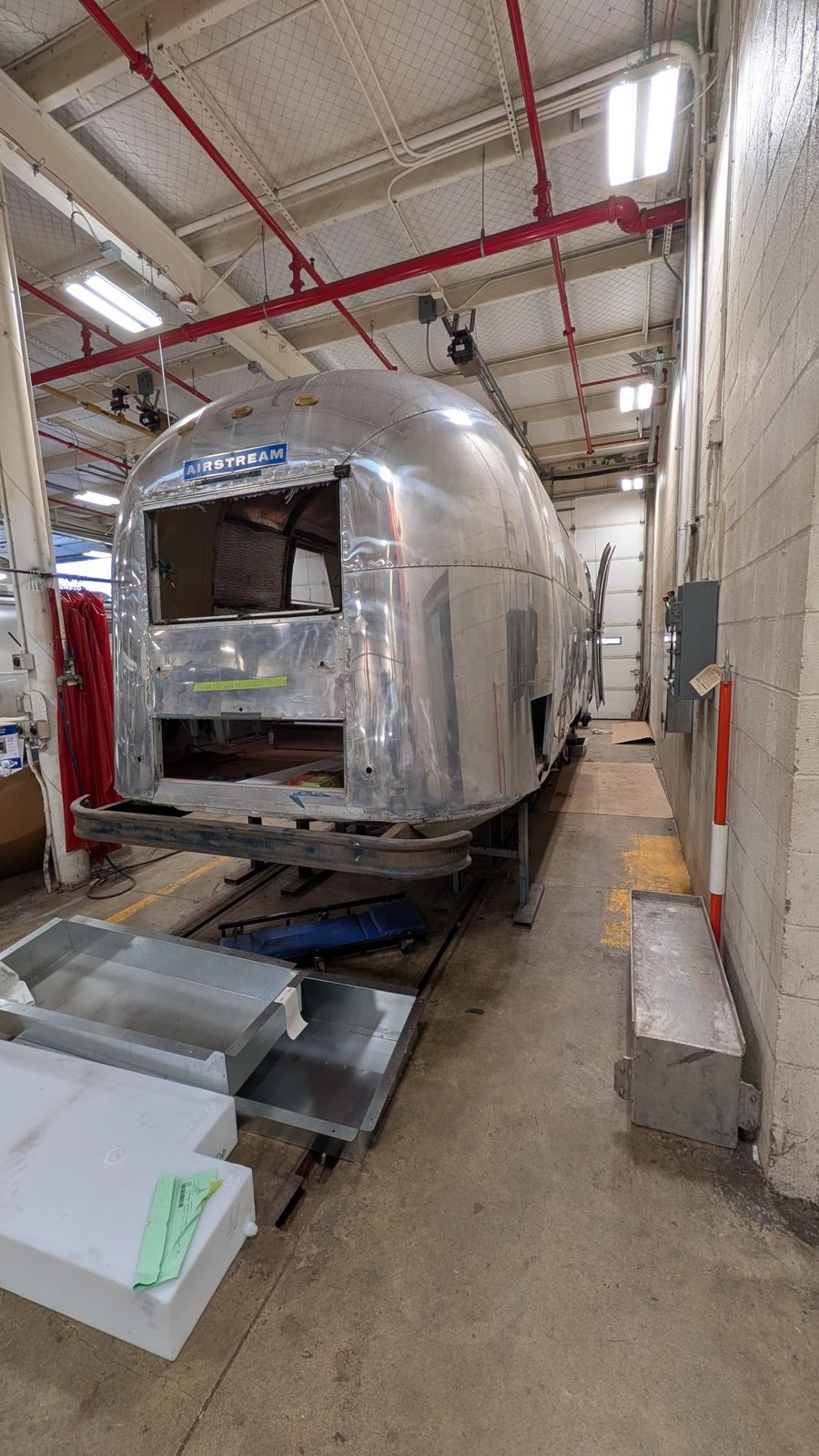 A three-quarter view of the Airstream's front from down the shop aisle, with openings in the shell where panels have been removed for the rebuild.