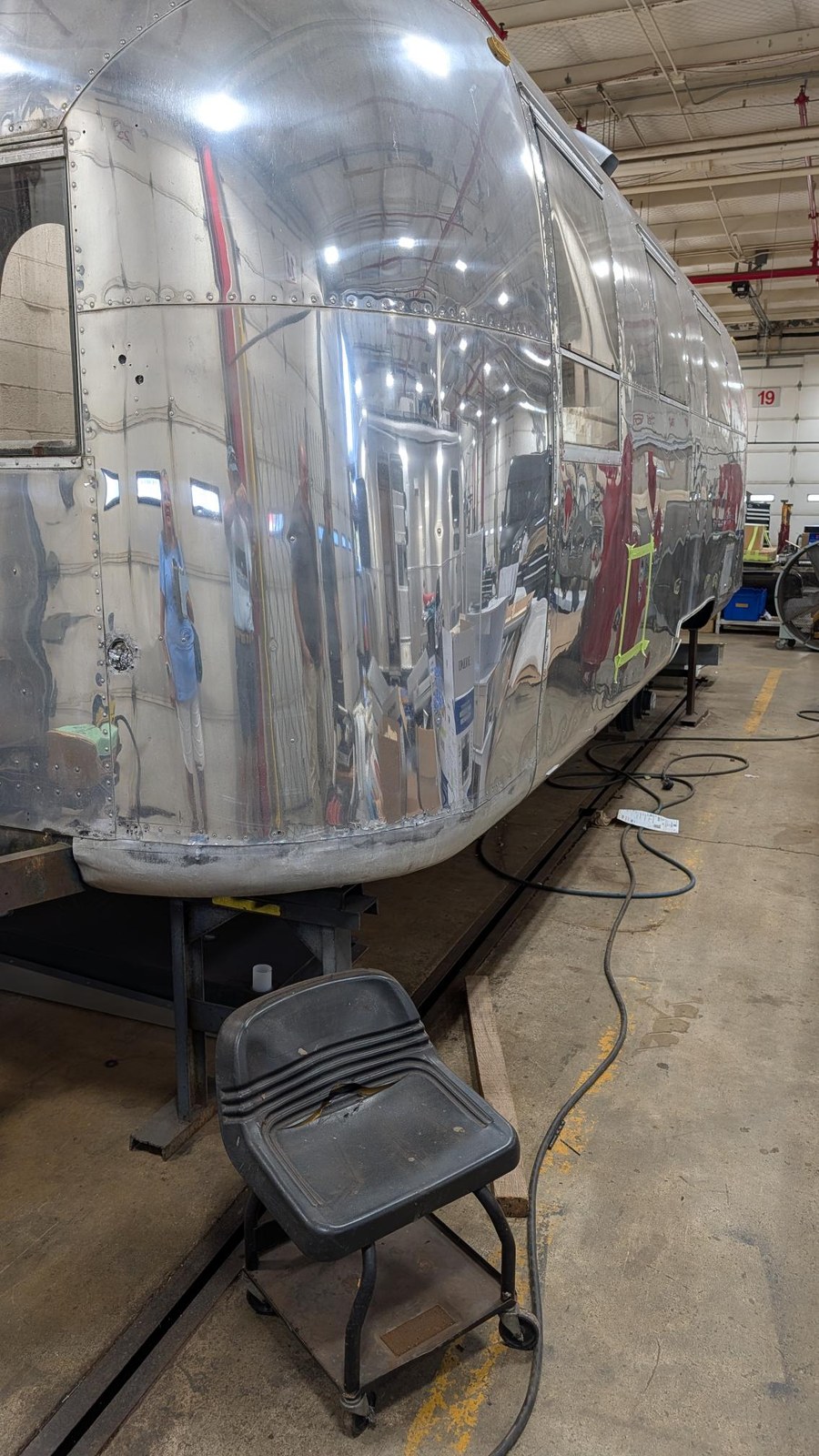 A long view down the polished curbside flank of the Airstream, riveted panels and windows running the length of the trailer.